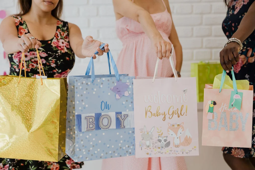 Pregnant women holding pink and blue paper gift bags at a baby shower