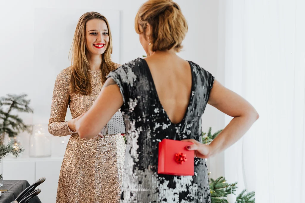 Two women exchanging wrapped gifts during a festive holiday celebration indoors