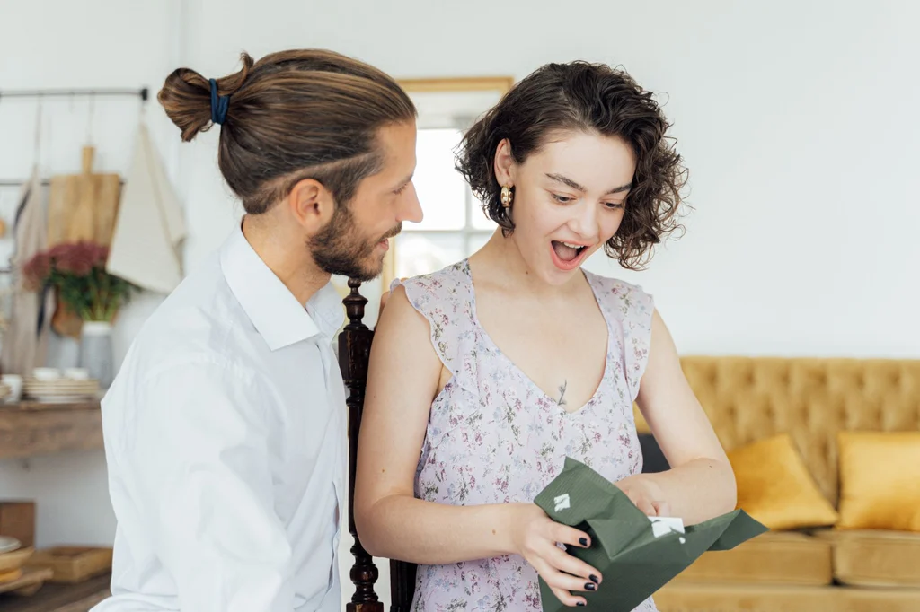 A couple opening a wrapped gift together indoors, surprised and delighted