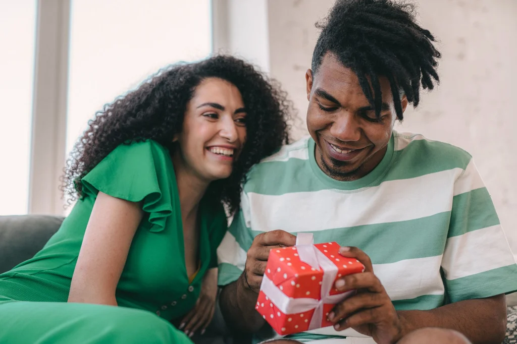 A young couple exchanging a wrapped gift at home — first wedding anniversary gift ideas (2026)