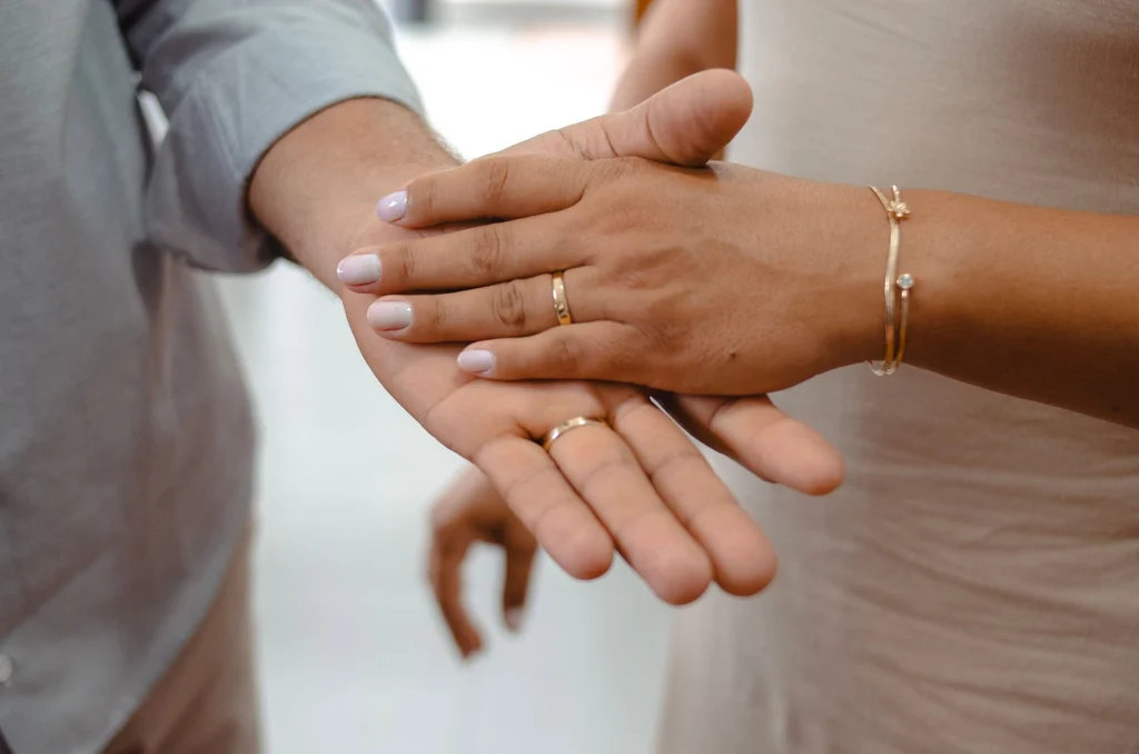 Close-up of a couple holding hands with wedding rings — third wedding anniversary gift ideas (2026)