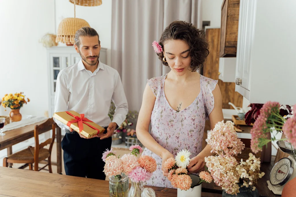 A couple in a cozy kitchen as the man offers a gift and the woman holds a bouquet of flowers, Mother's Day gifts for your wife (2026)